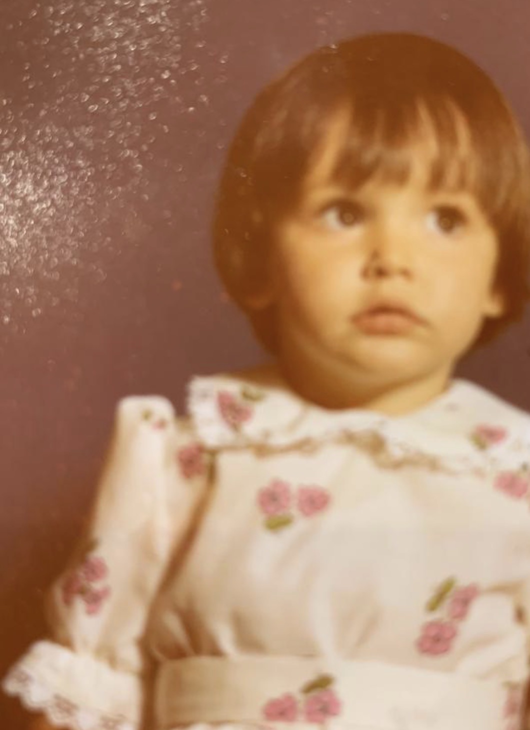 Claire Marshall as a young child in a white dress with pink flowers